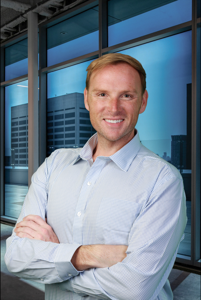 Portrait of a smiling man in a tan blazer and white shirt against a blue background