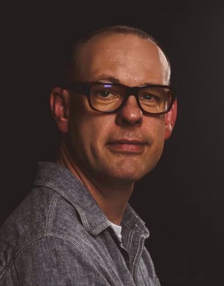 Portrait of a man wearing glasses and a gray shirt against a dark background