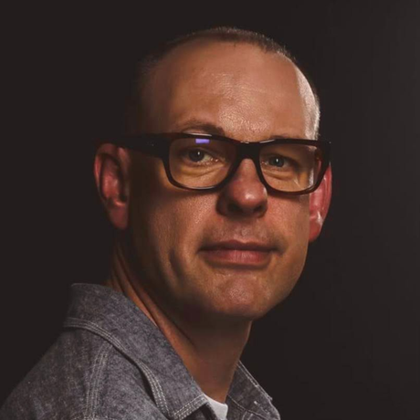 Portrait of a man wearing glasses and a gray shirt against a dark background