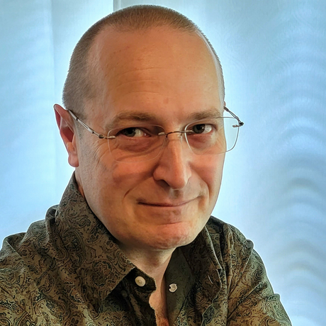 Portrait of a man in glasses and a patterned shirt, smiling against a light blue background