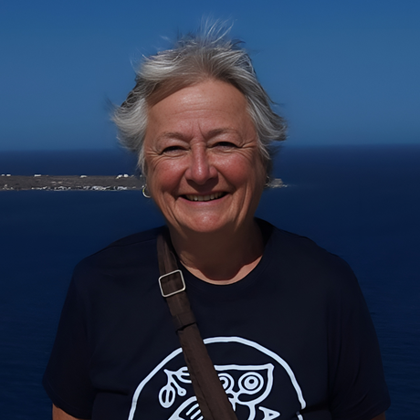 Smiling person in a navy shirt standing by the ocean under a clear blue sky.