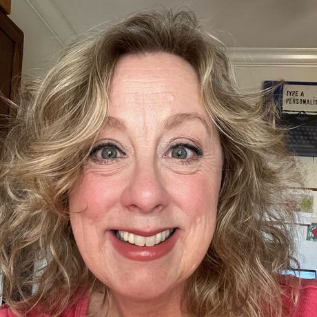 Smiling woman with wavy blond hair indoors, close-up selfie in soft natural light