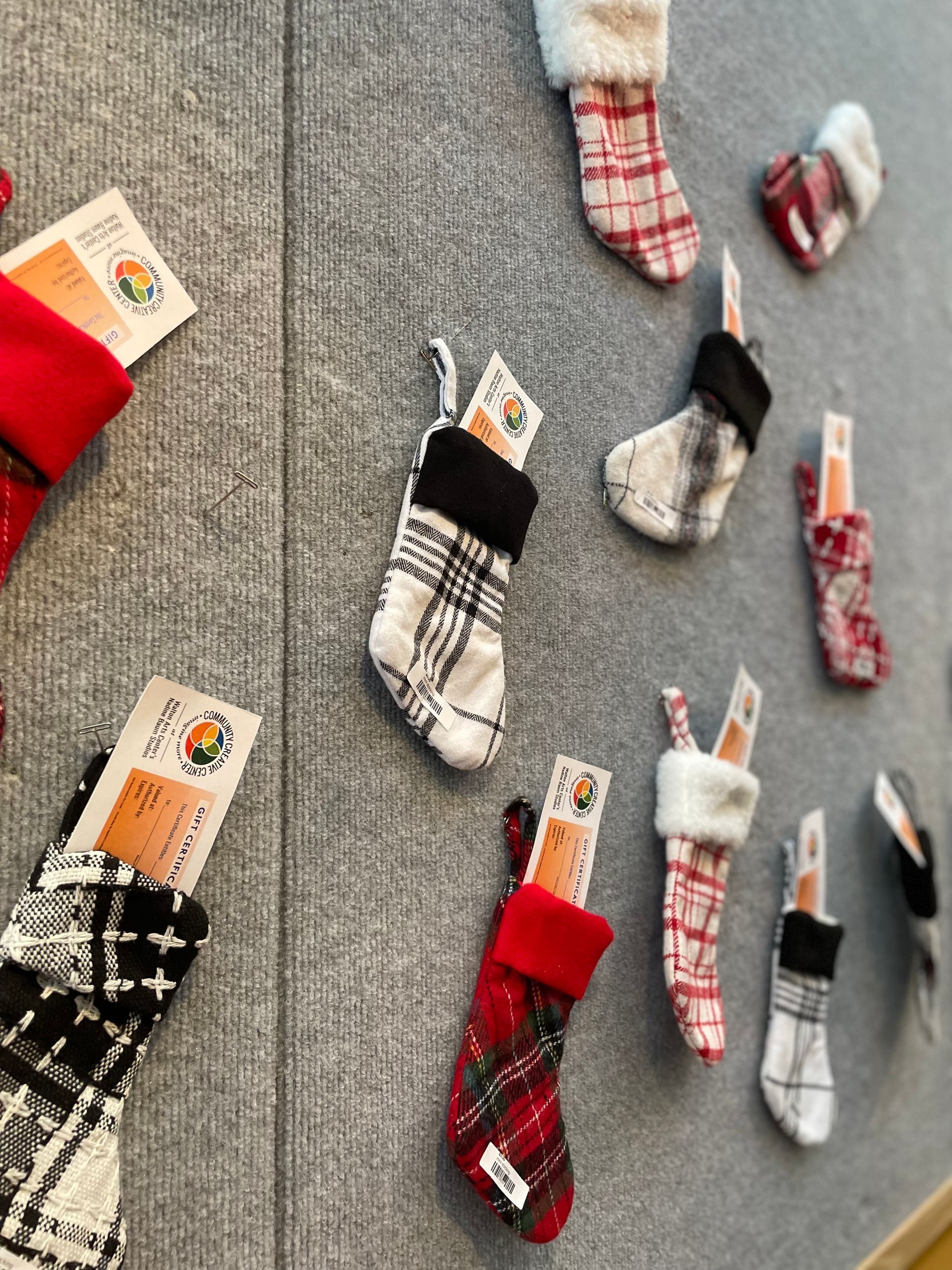 Assorted Christmas stockings hanging on a gray wall, featuring red, white, black, and plaid patterns.
