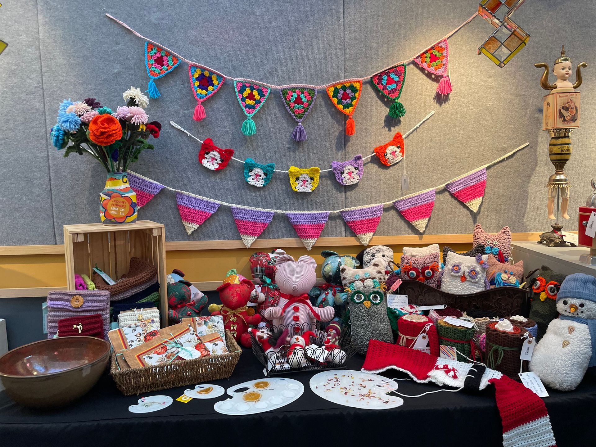 Colorful display of handmade crafts, flowers, and plush toys arranged on a table with festive hanging garlands