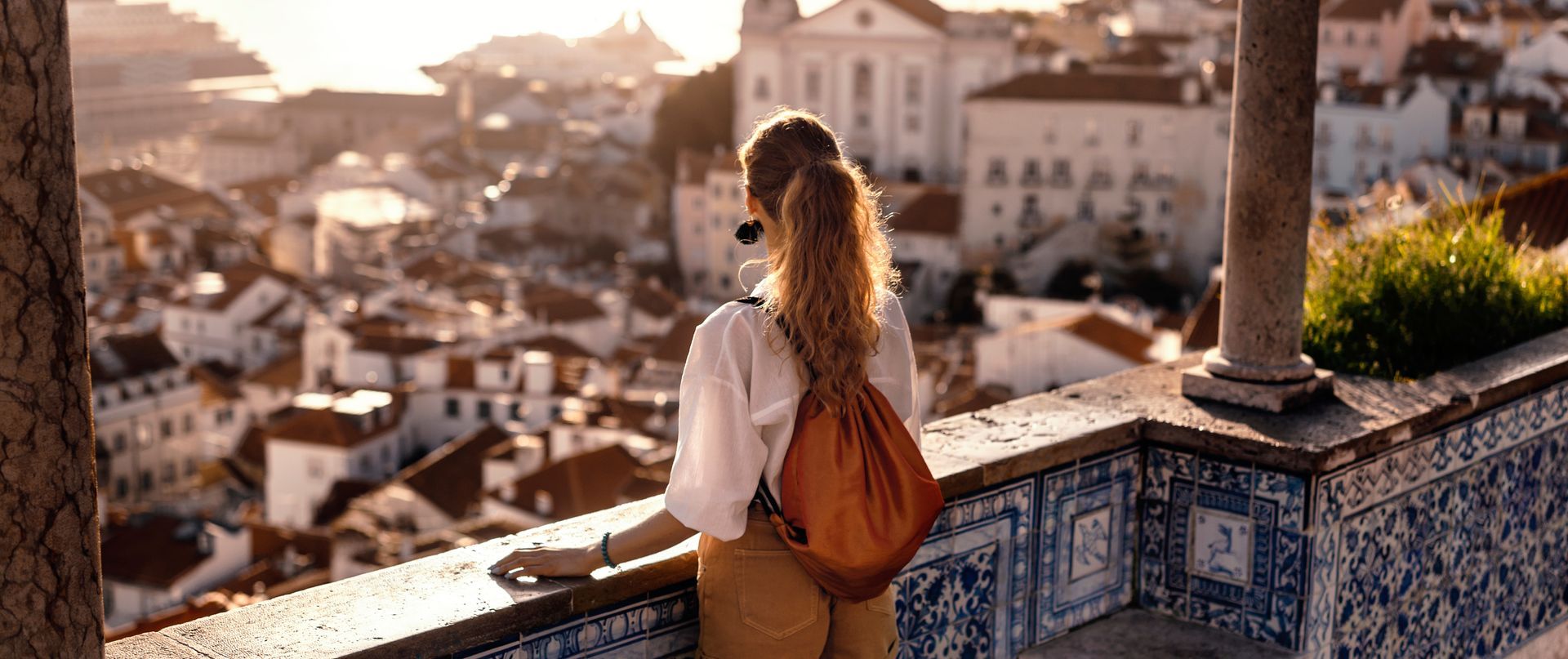 A woman with a backpack is standing on a balcony overlooking a city.