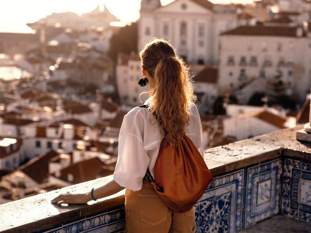 A woman with a backpack is standing on a balcony overlooking a city.
