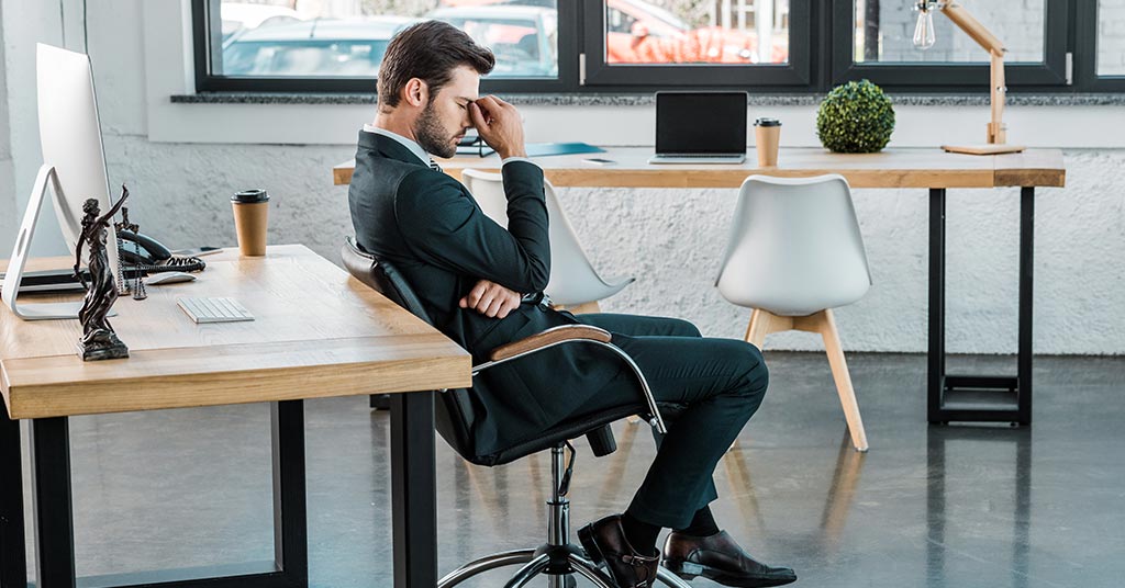 Homem de terno, estressado, sentado à mesa em um escritório moderno.