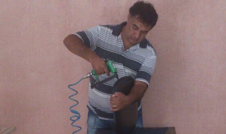 Homem usando um grampeador em um objeto preto, possivelmente estofado. Ele está vestindo uma camisa listrada e calça jeans.