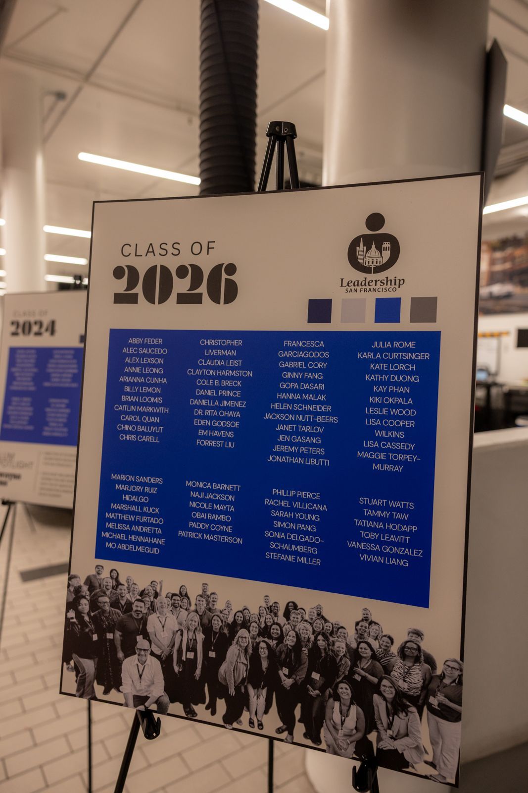 Class of 2026 poster on an easel with blue text and a black-and-white group photo at bottom in a lobby