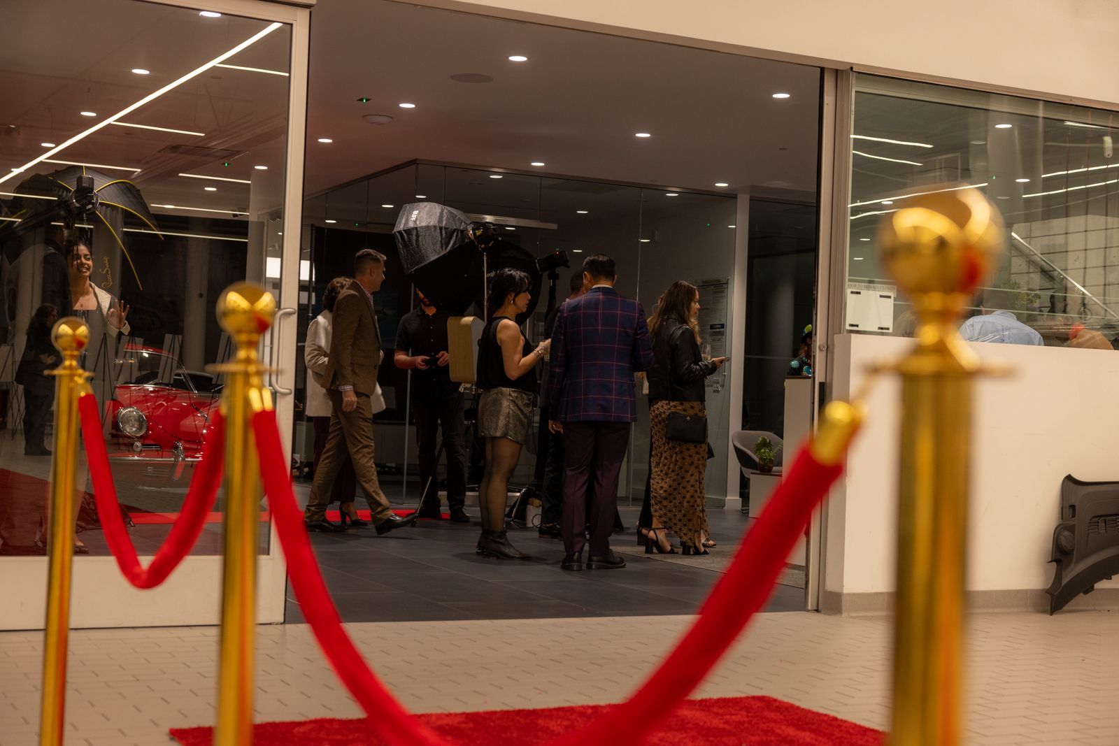 People standing behind a red rope barrier at an indoor event entrance.