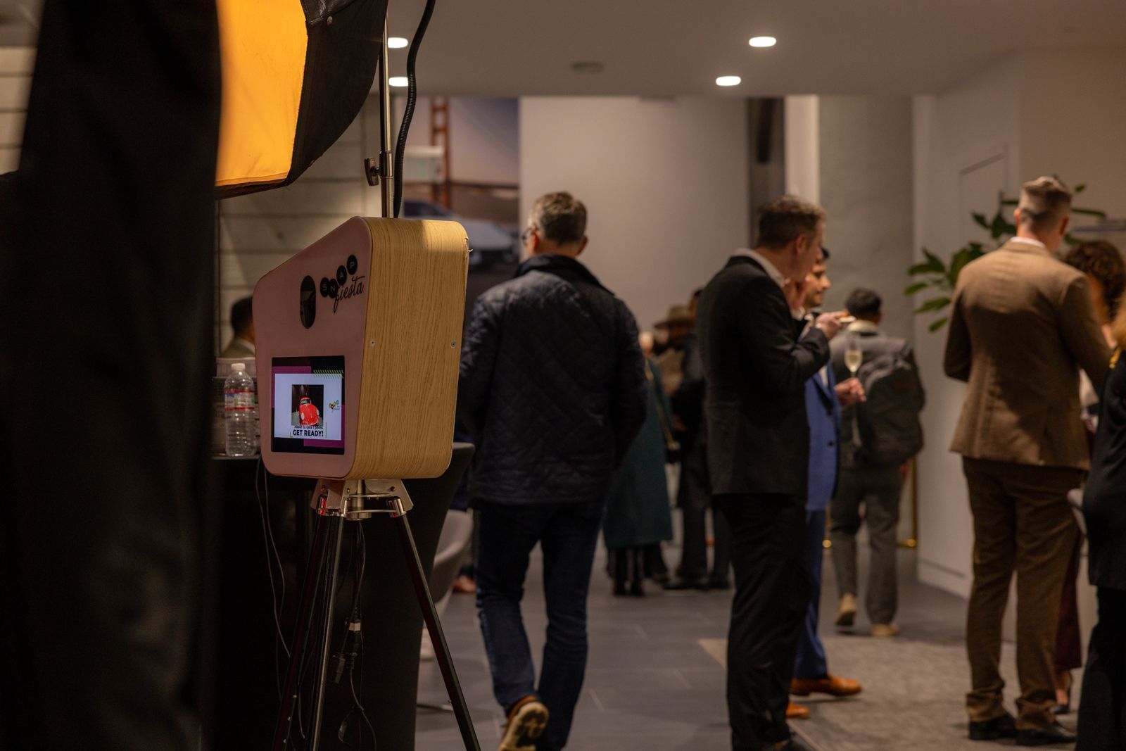 People standing in a hallway near a photo booth and display screen at an indoor event