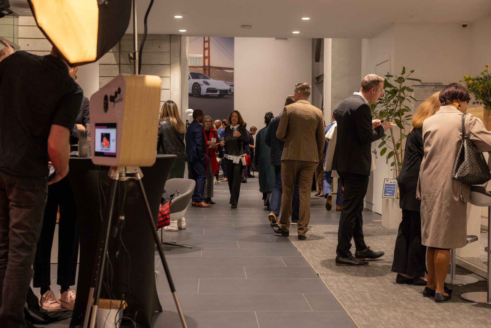 People standing in a hallway at an indoor event, with cameras and coats visible.