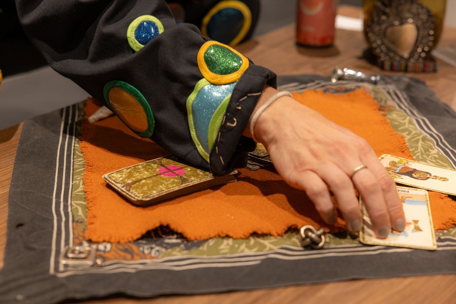 Hand placing cards on an orange cloth on a wooden table during a card reading.