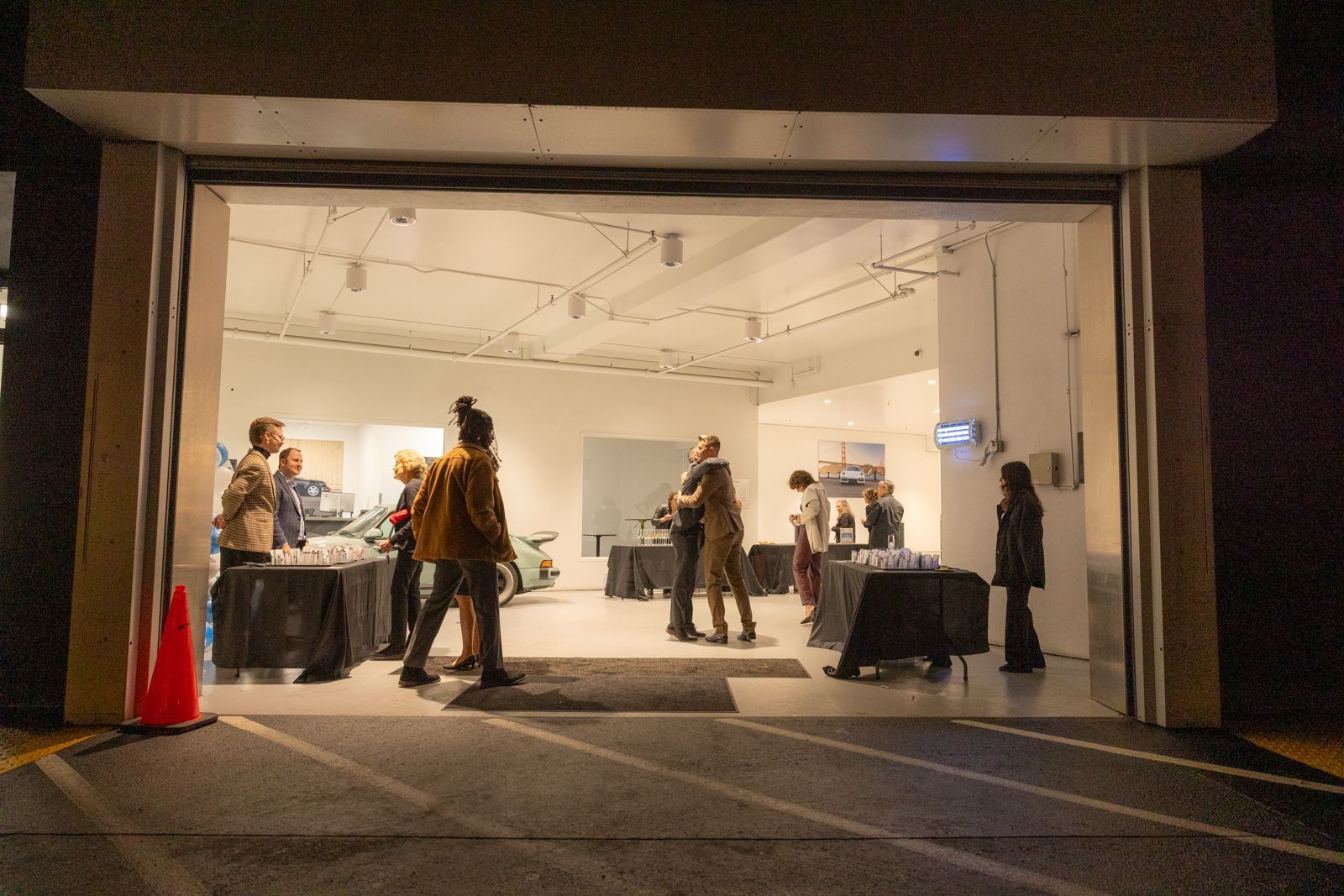 People standing in a brightly lit gallery space, seen through a wide open doorway at night.