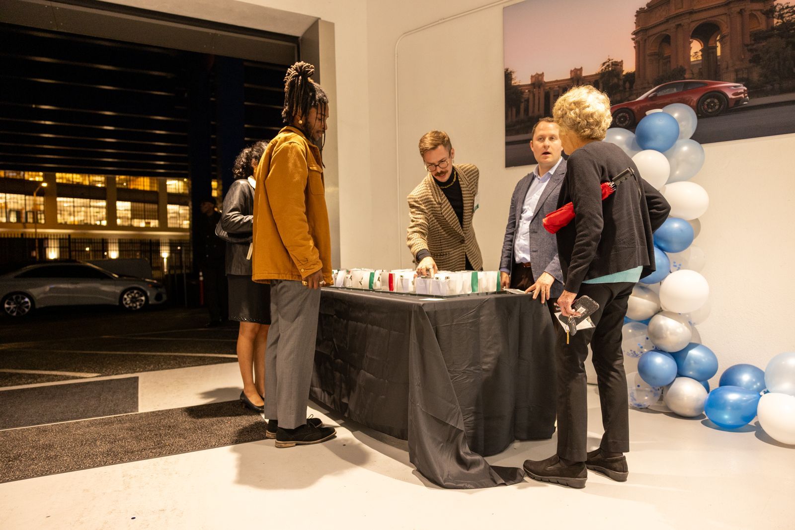 People gathered around a table at an indoor event, beside blue-and-white balloon decorations.