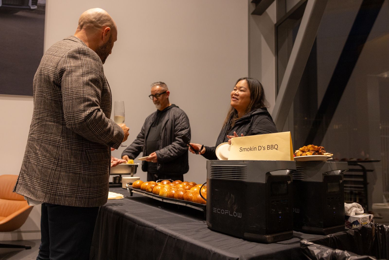 People at a buffet table serving drinks and snacks in a dim indoor event space