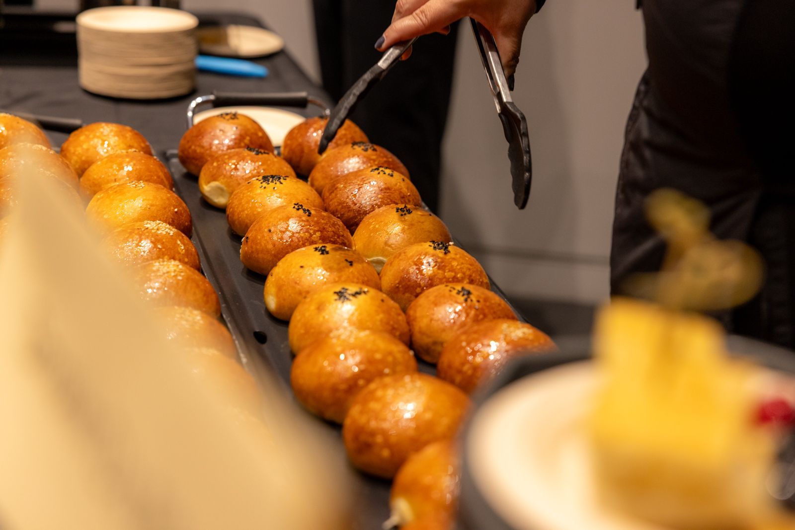 Hand placing tongs over rows of glazed doughnuts on a bakery display tray