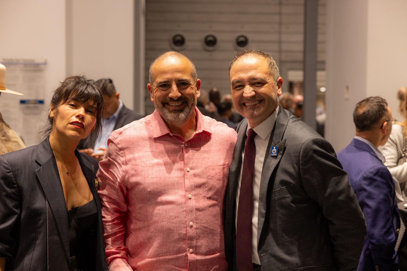 Three people posing indoors at an event, smiling at the camera, with two in button-down shirts and one in a blazer.