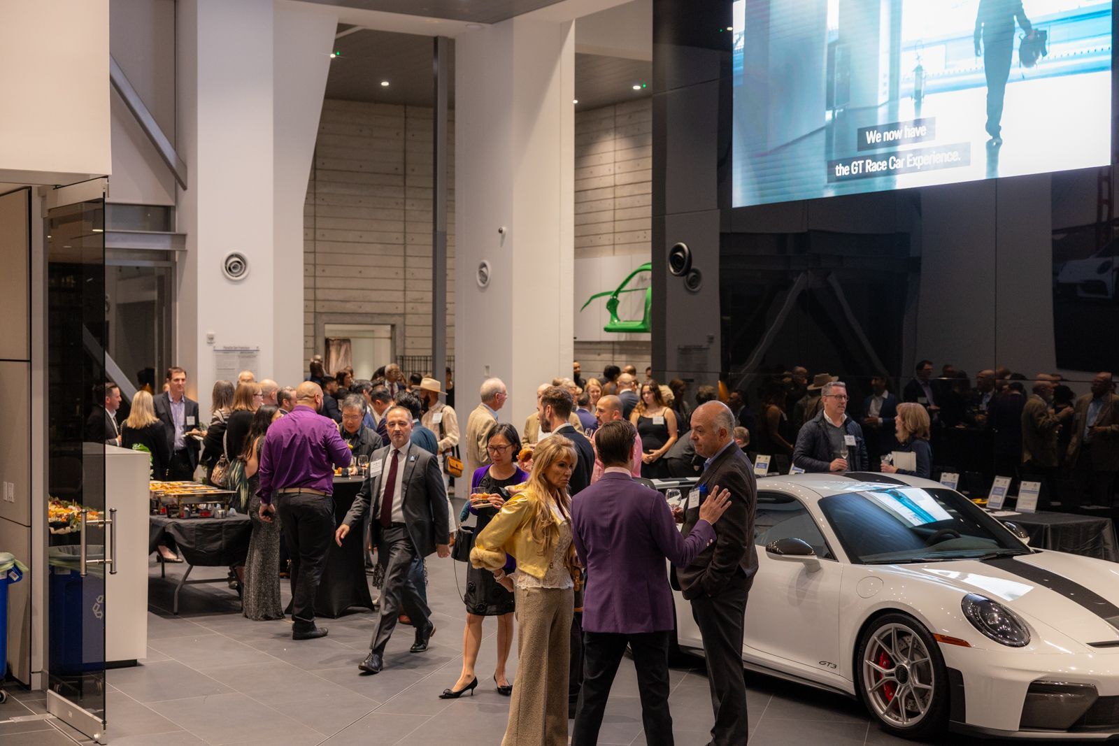 Crowd at an indoor auto show beside a white sports car under bright lights.