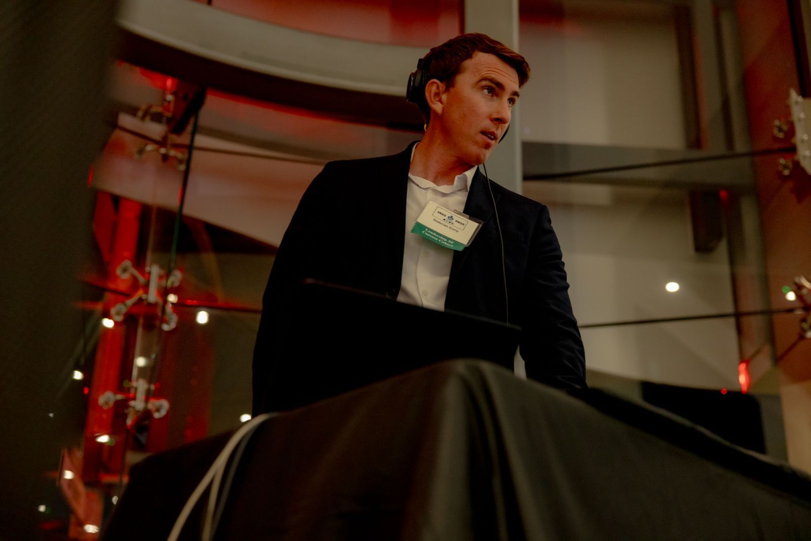 Man standing by a covered object in a dim red-lit room, looking to the side.