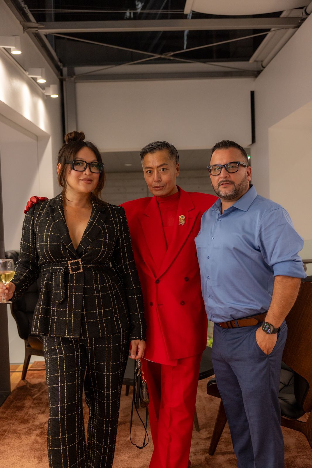 Three people posing indoors, including one in a red suit and one in a blue shirt.