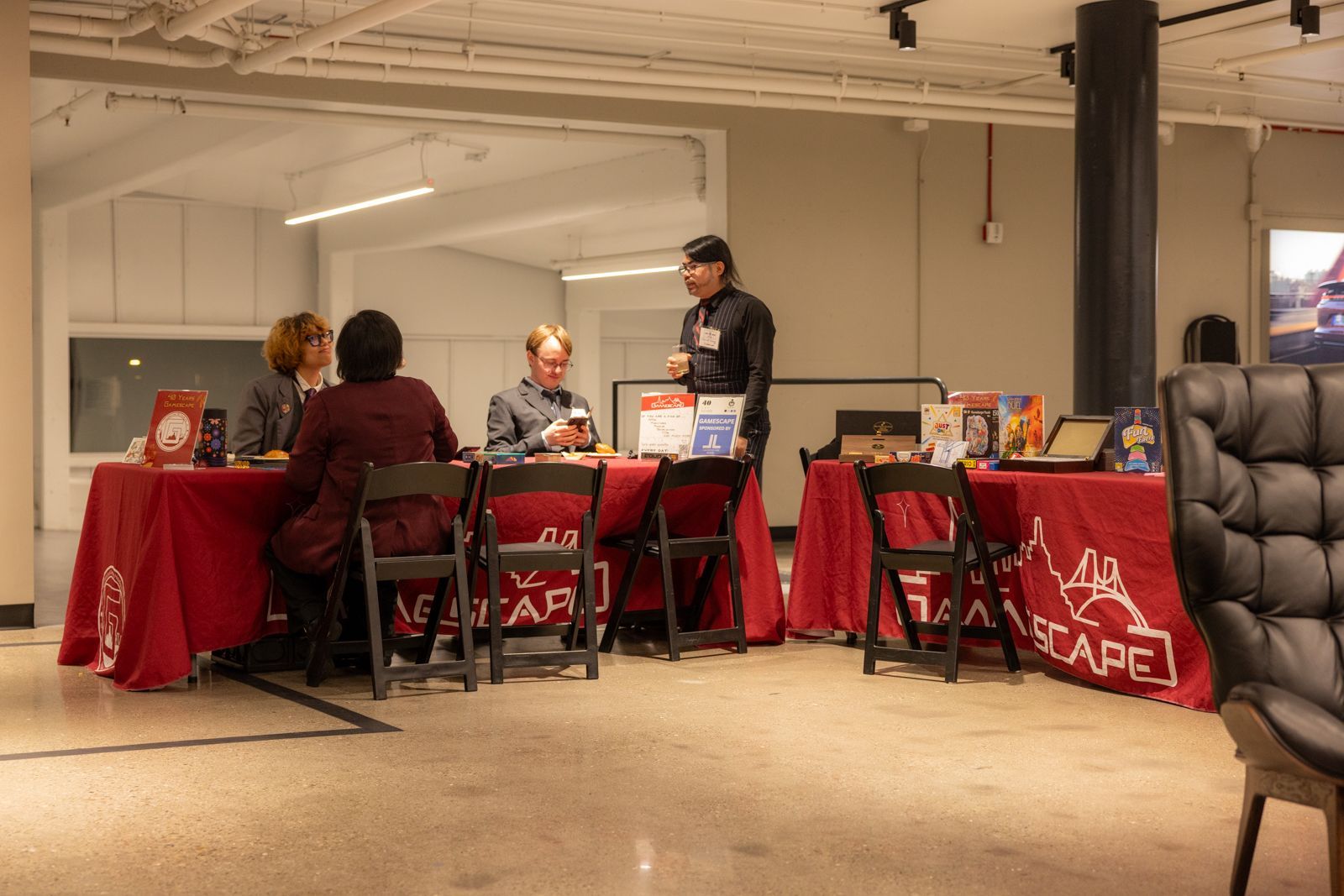 People at a red-draped cafe booth in a bare indoor room, with menus and a sofa on the right