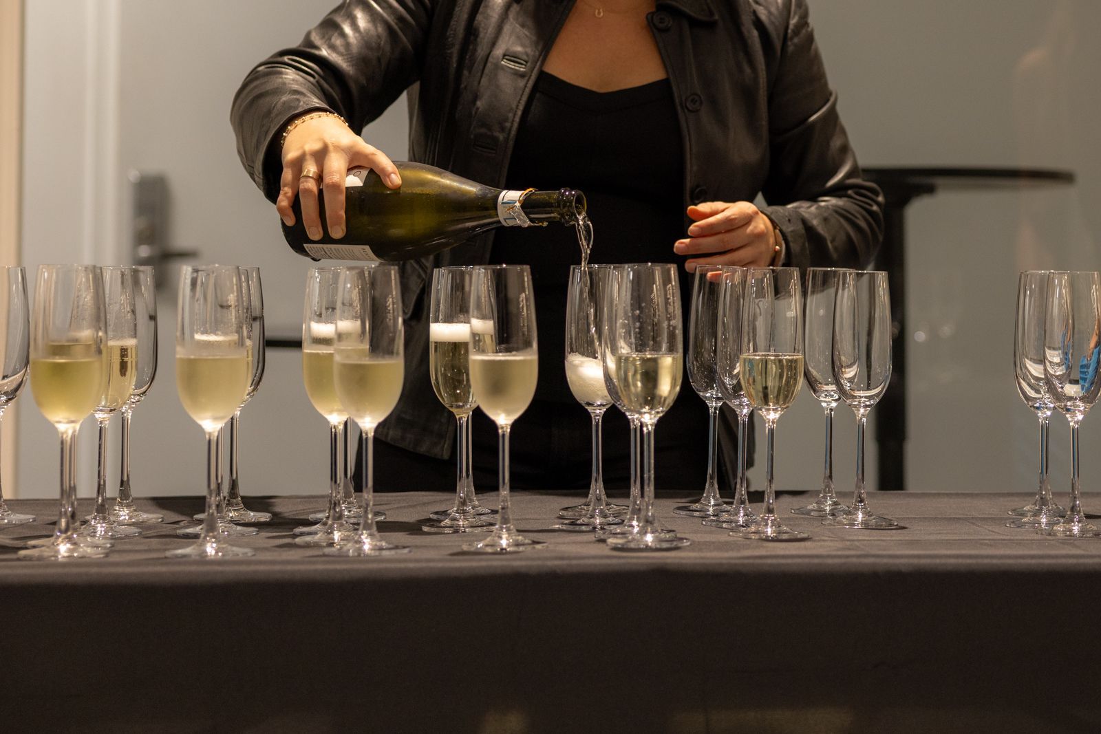 Person pours champagne into a row of flute glasses at a bar setup.