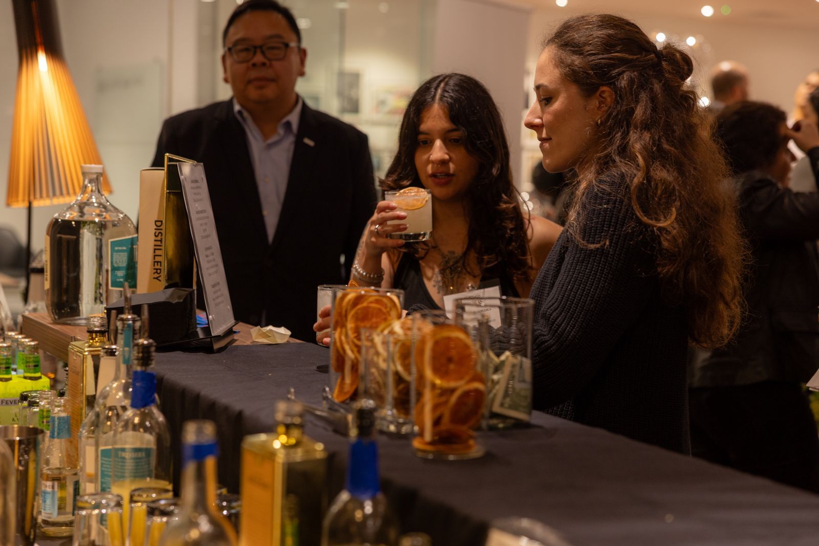 People sampling drinks at a dimly lit bar with bottles lined up on the counter