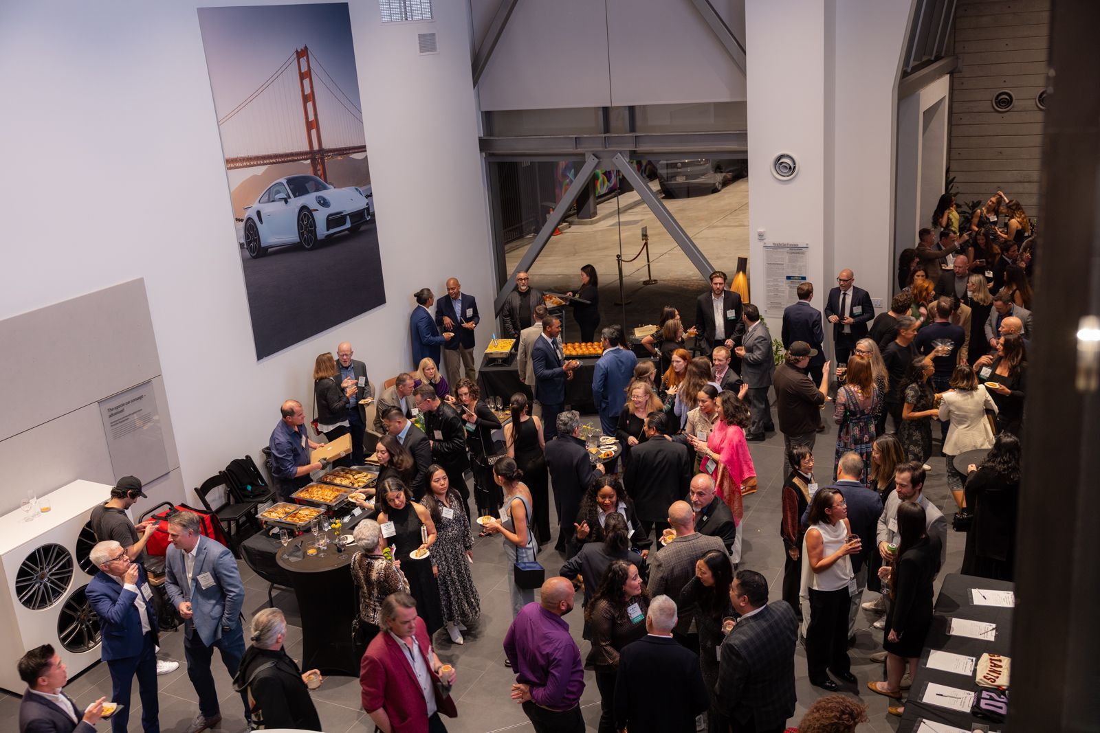 Crowded indoor event with people mingling around tables in a bright lobby-like space