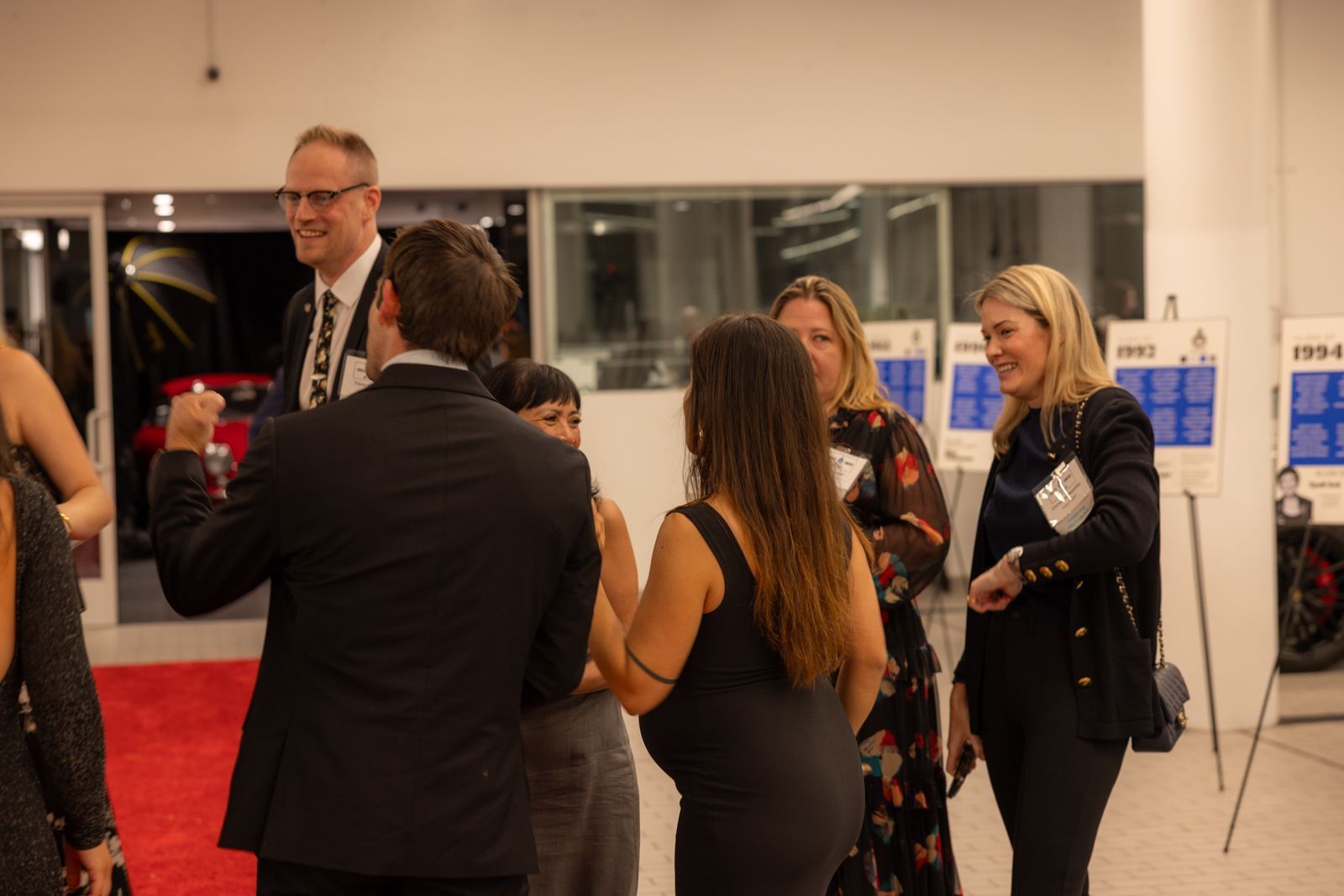 People chatting at a formal indoor reception with a red carpet and art displays.