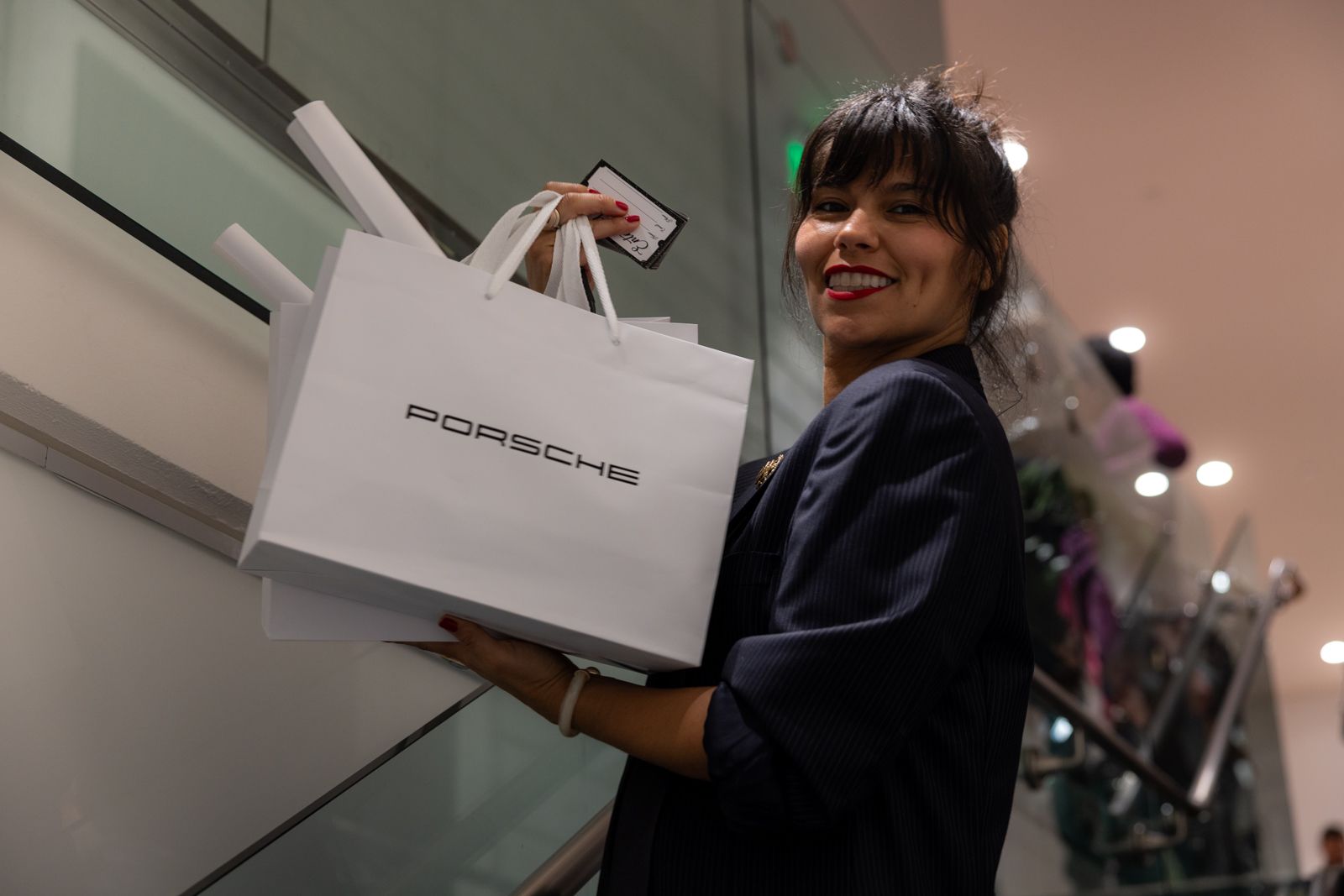 Woman carrying a large white shopping bag on an escalator, smiling in a mall.