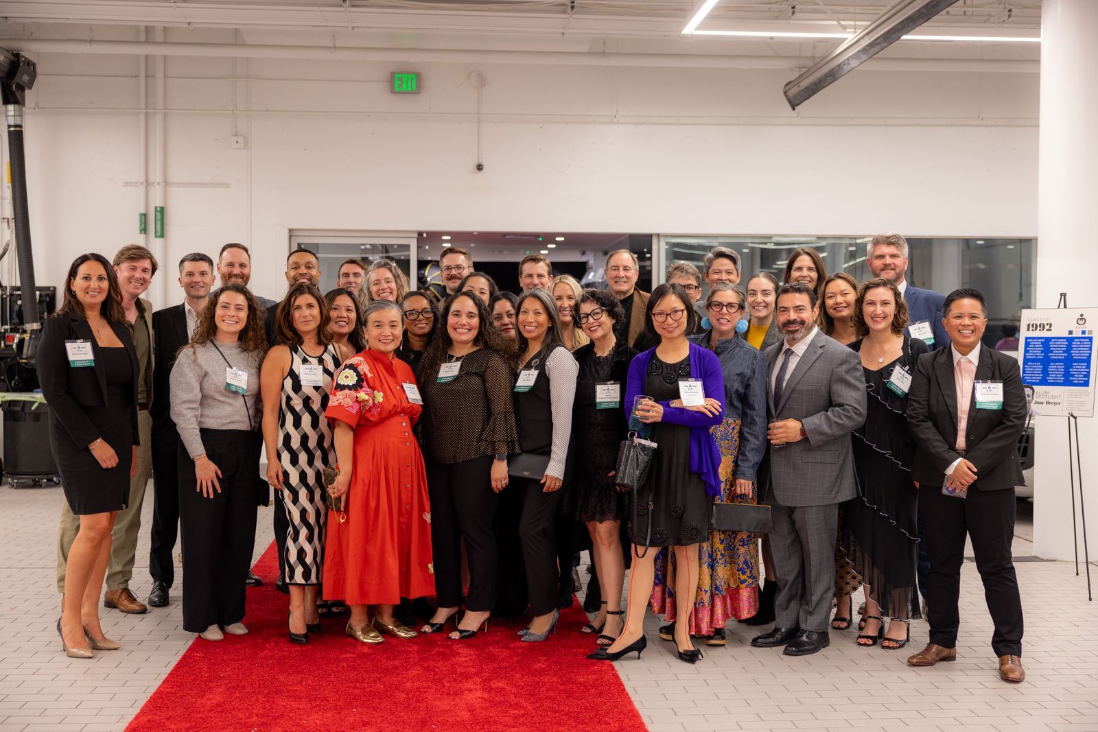 Group of people posing indoors on a red carpet at a formal event, with a photo backdrop behind them