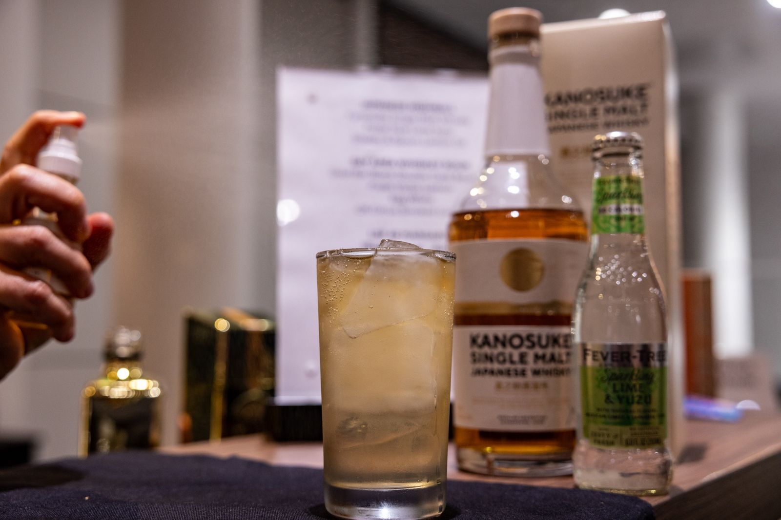 Whiskey bottle and glass on a bar, with a hand spraying mist beside them