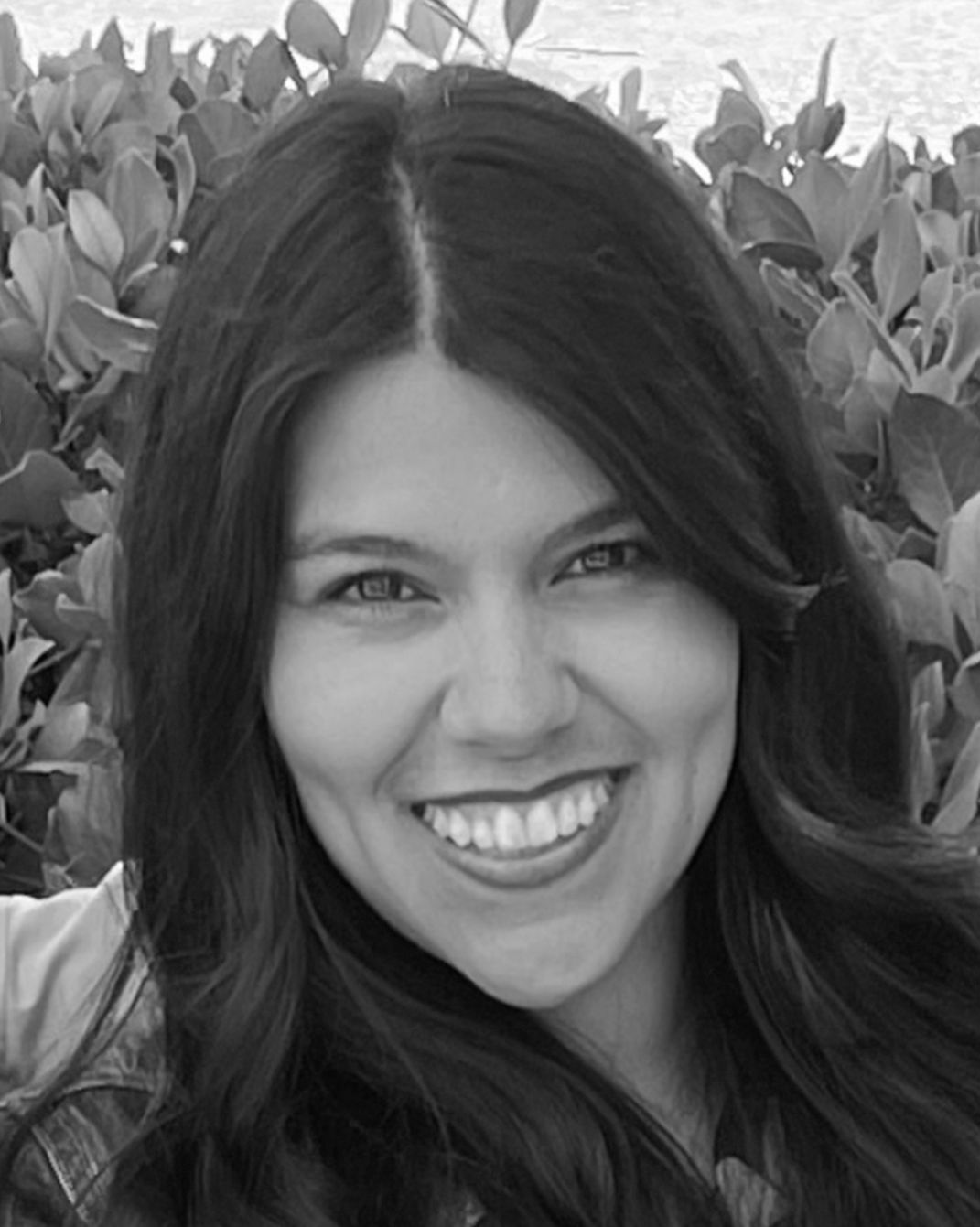 Smiling woman with long dark hair in front of leafy greenery