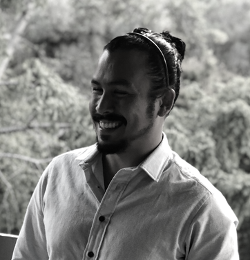 Smiling person in a light shirt, standing outdoors with blurred trees in the background