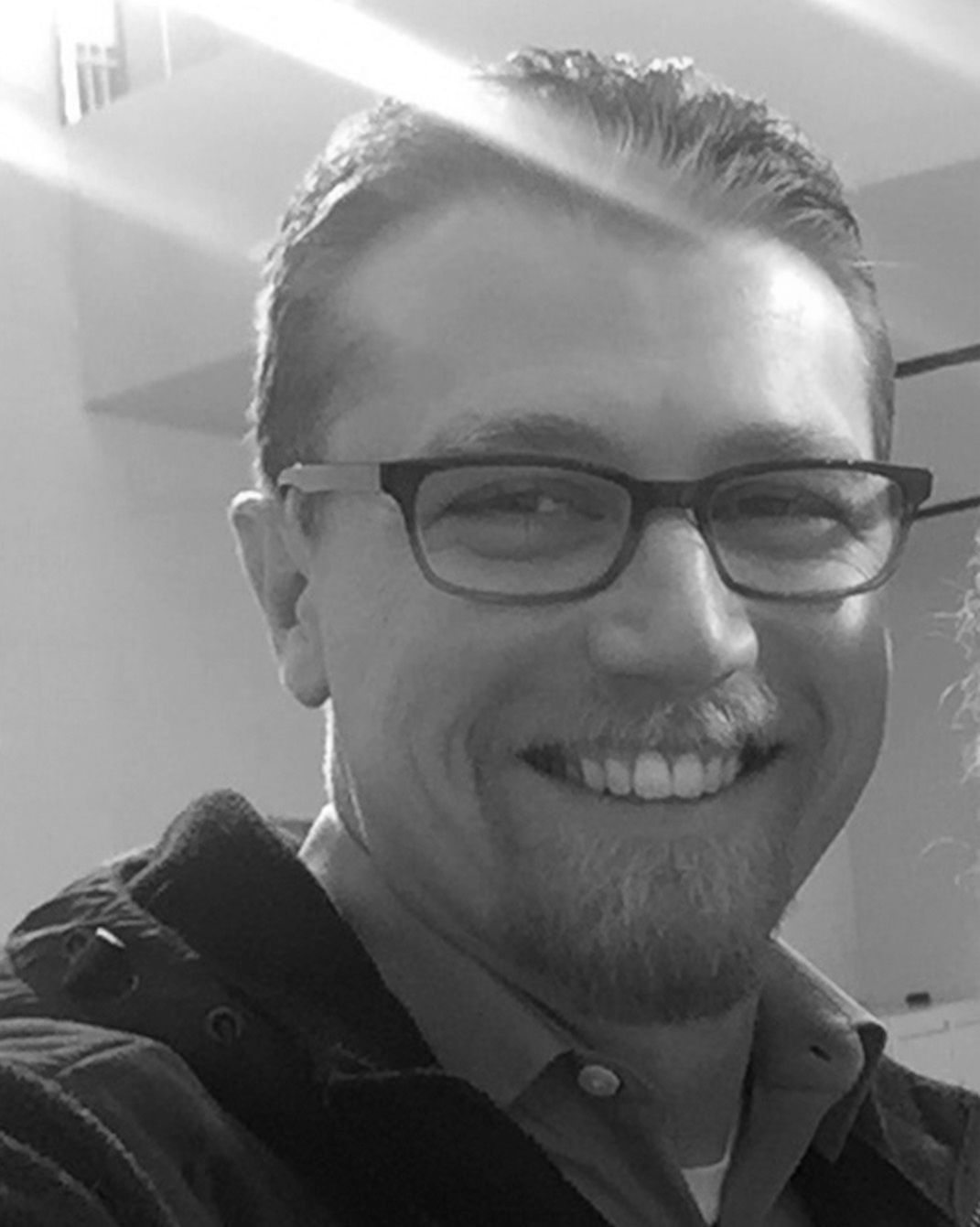 Smiling person wearing glasses in a black-and-white portrait