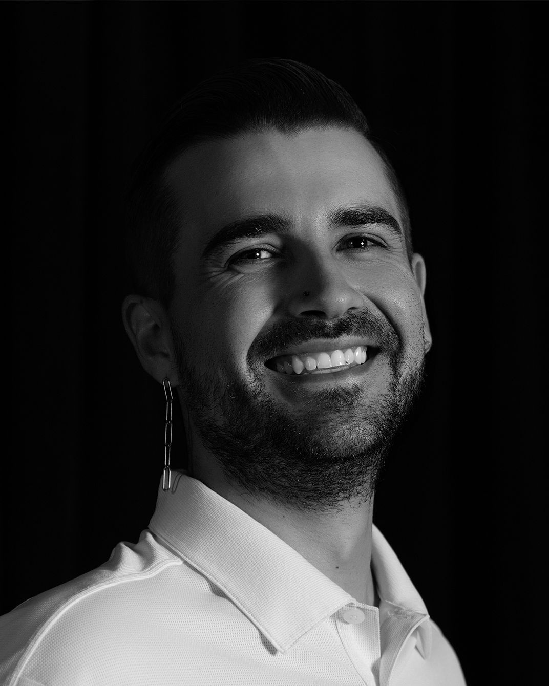 Smiling person in a white collared shirt against a dark background
