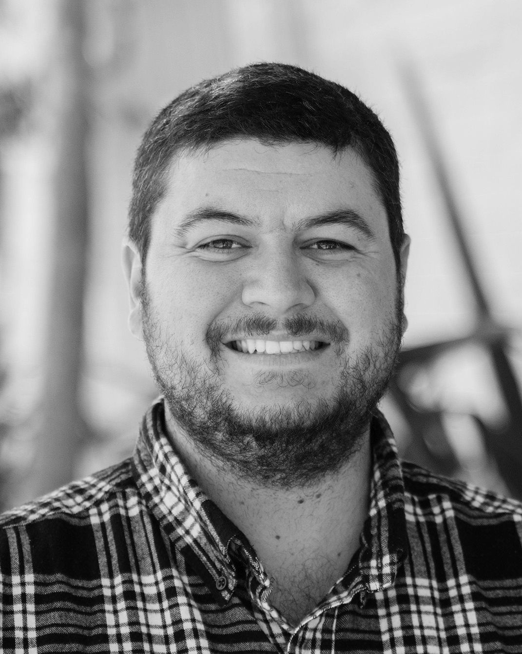 Smiling man in a plaid shirt, photographed in black and white.
