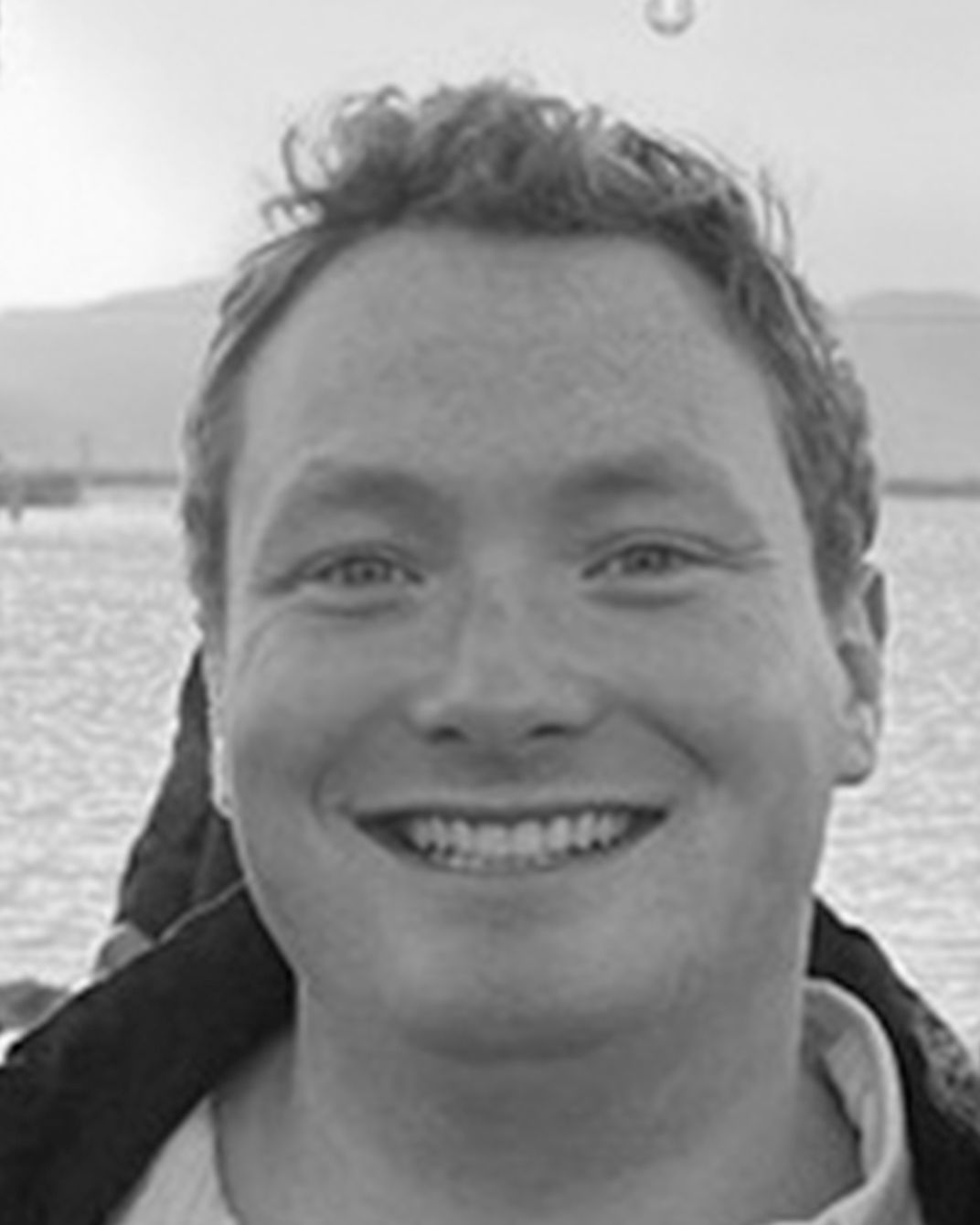 Smiling person in a jacket with water and hills in the background