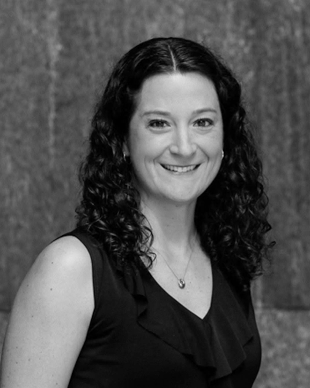 Smiling woman in a sleeveless black top against a textured backdrop