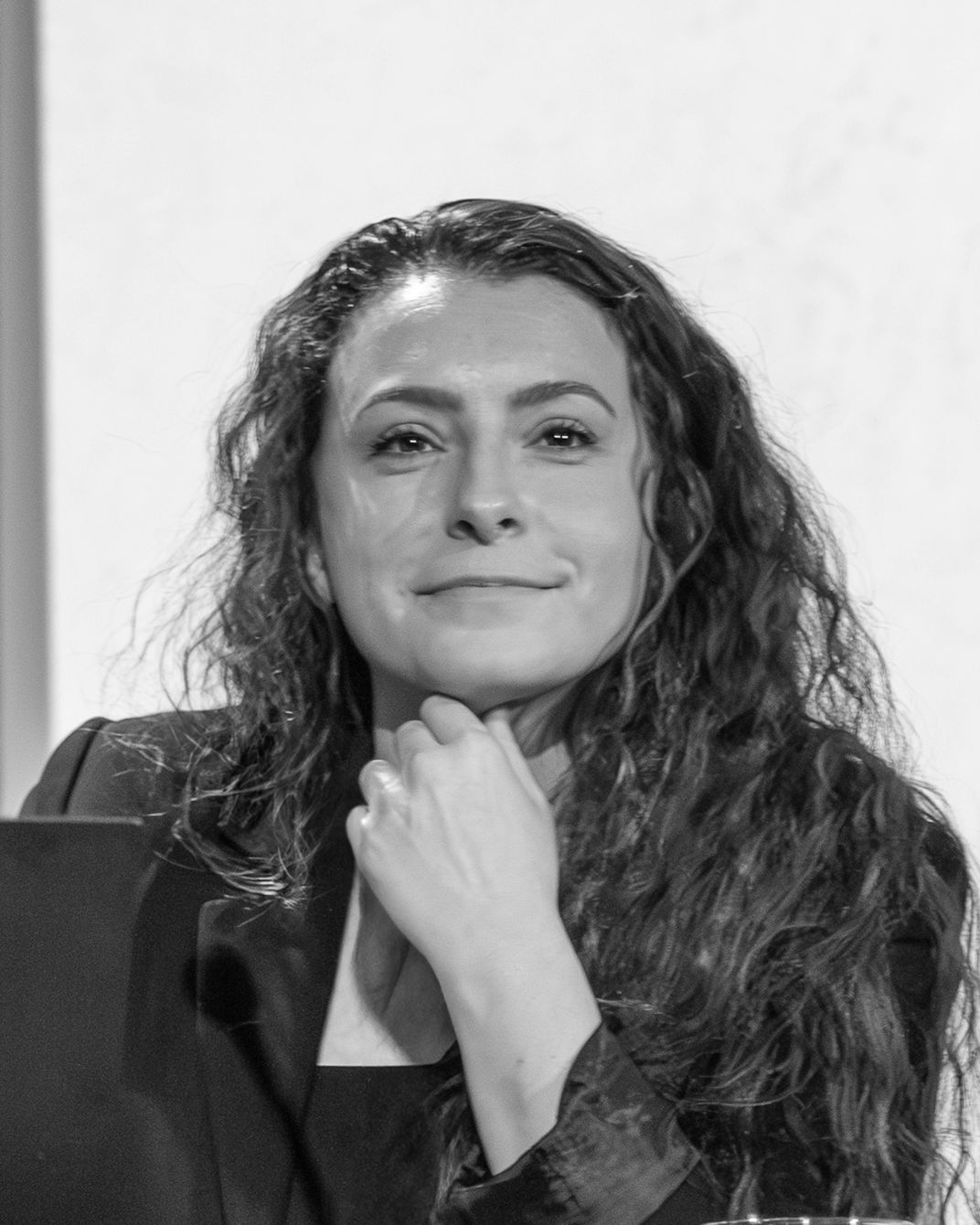 Woman with long curly hair resting her chin on her hand, seated in front of a microphone.