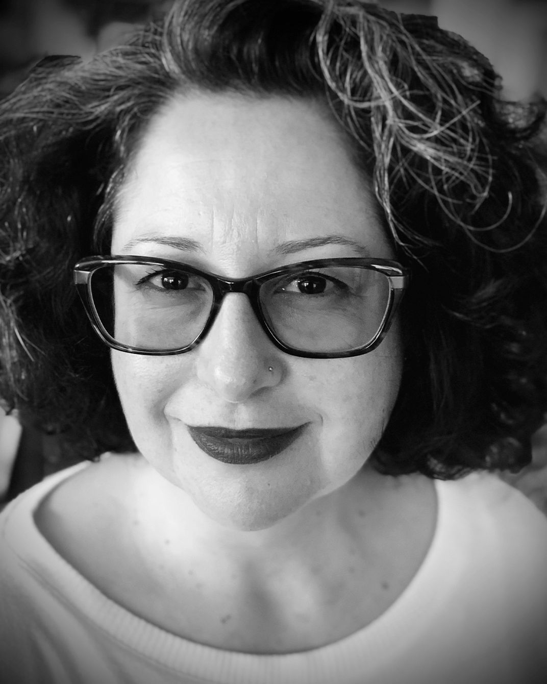 Black-and-white close-up portrait of a person with glasses and curly hair, smiling softly