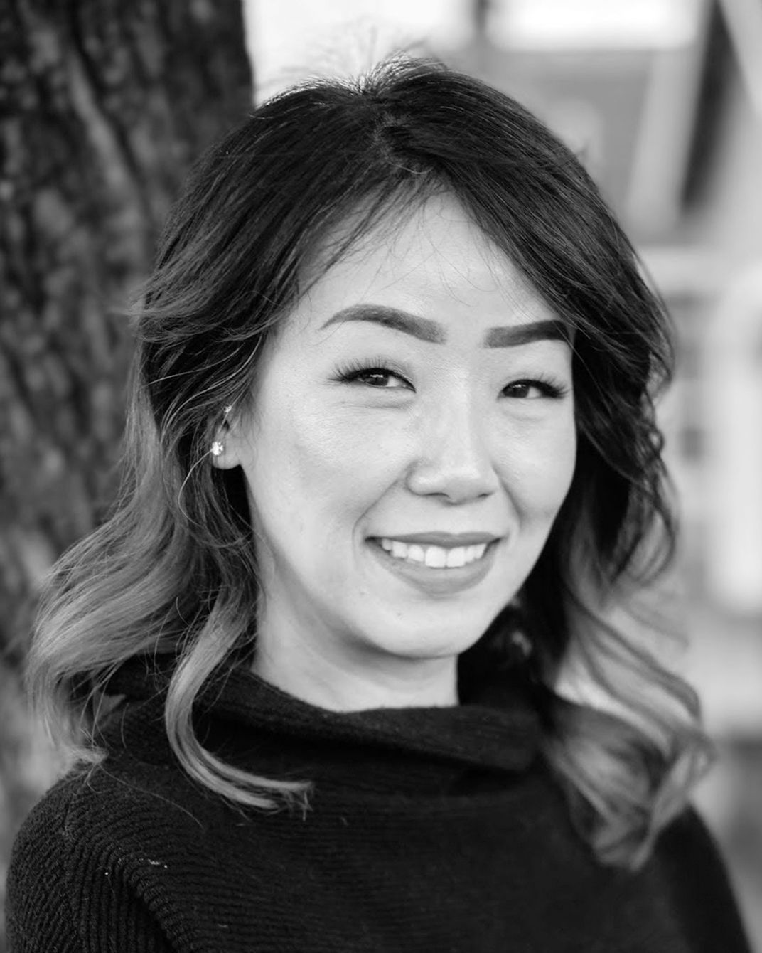 Smiling person in a dark sweater, photographed outdoors in black and white.