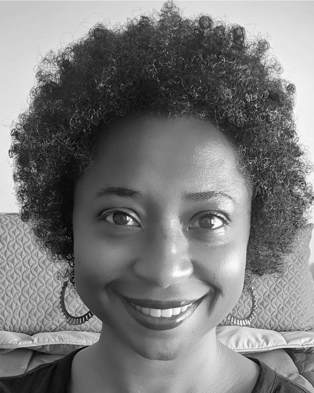 Smiling person in black-and-white portrait, seated indoors against a patterned couch