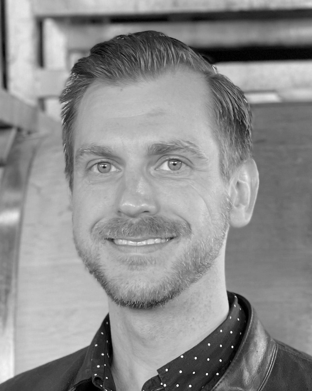 Black-and-white portrait of a smiling man in a patterned shirt and jacket
