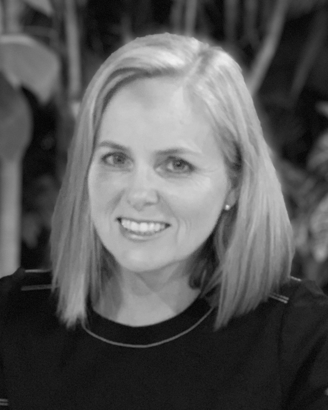 Smiling blonde woman in a dark top against a blurred black-and-white background