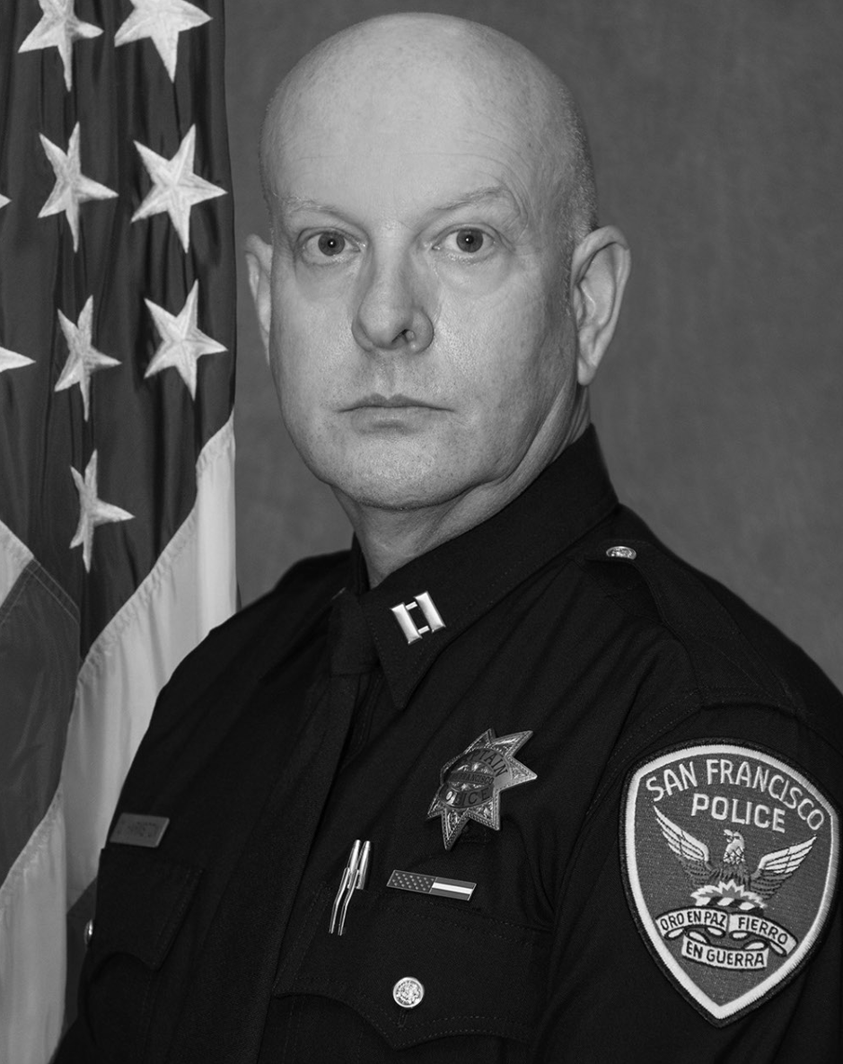 San Francisco police officer in uniform posing before a U.S. flag and plain backdrop