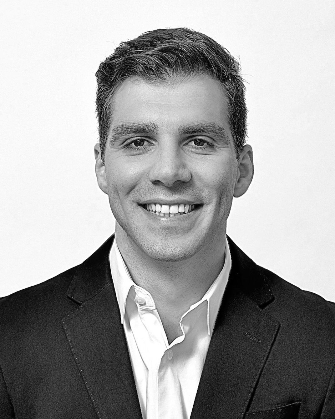 Smiling man in a dark blazer and white shirt against a light background