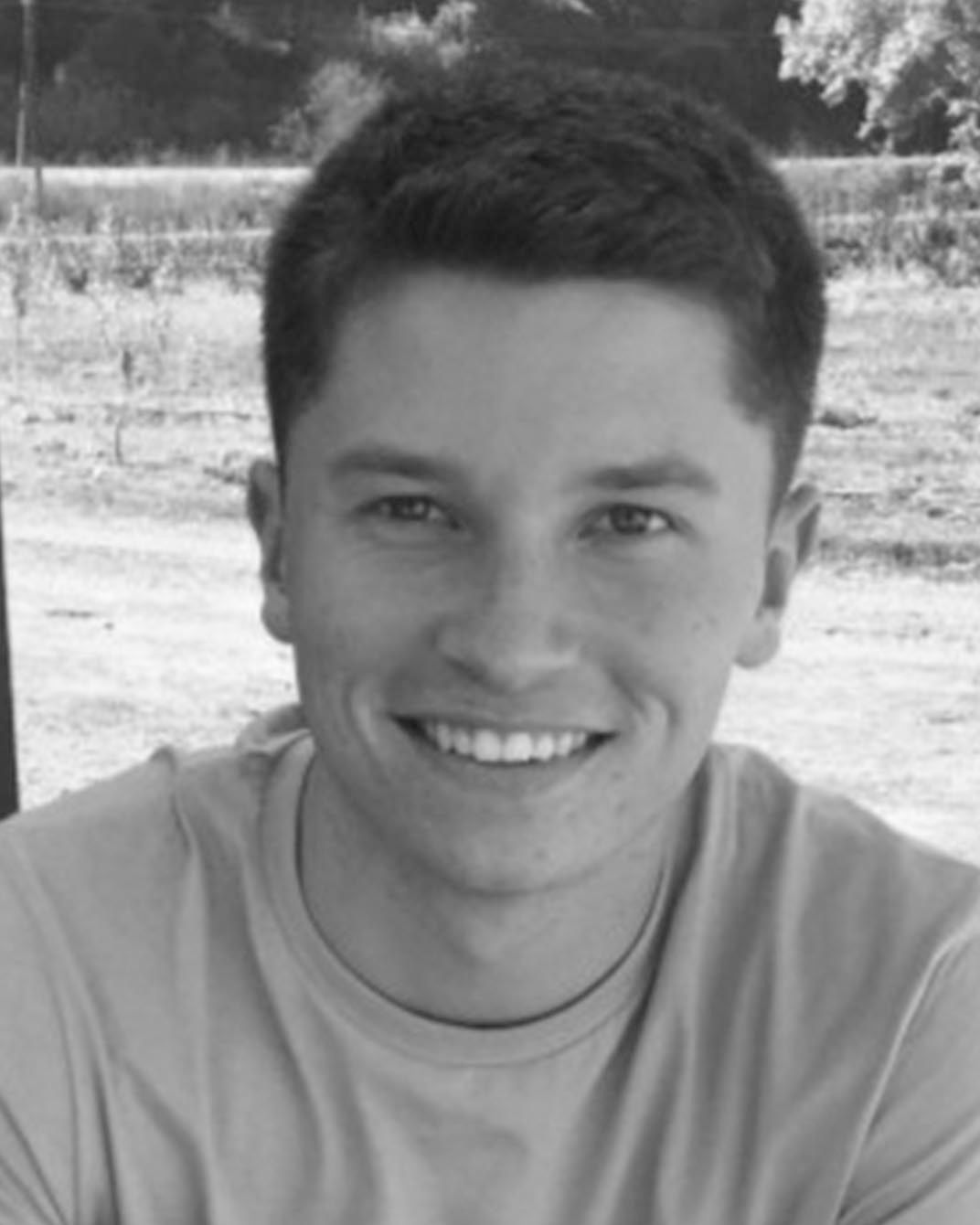 Smiling person in a light shirt outdoors, with a blurred background.