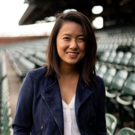 Smiling woman in a navy jacket standing in empty stadium seats